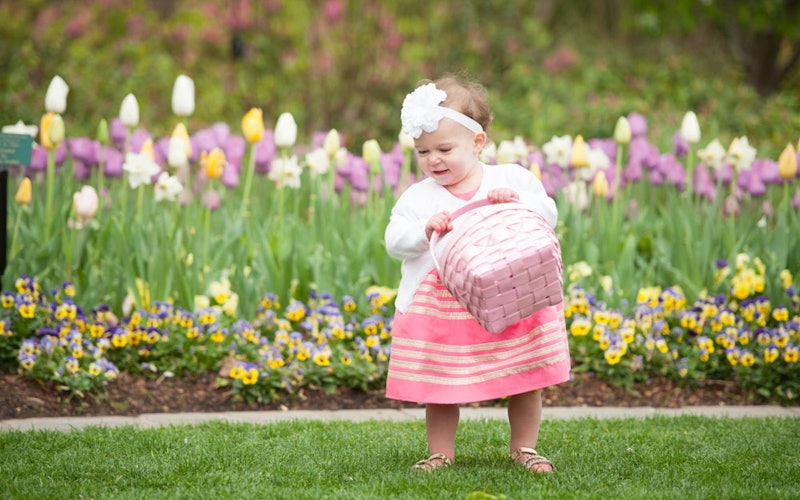 A little girl with an Easter basket searching for eggs in the garden.